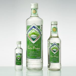 Fotografia de três garrafas de difrentes tamamanhos da cachaça pedra branca amendoim premium. Fim da descrição.